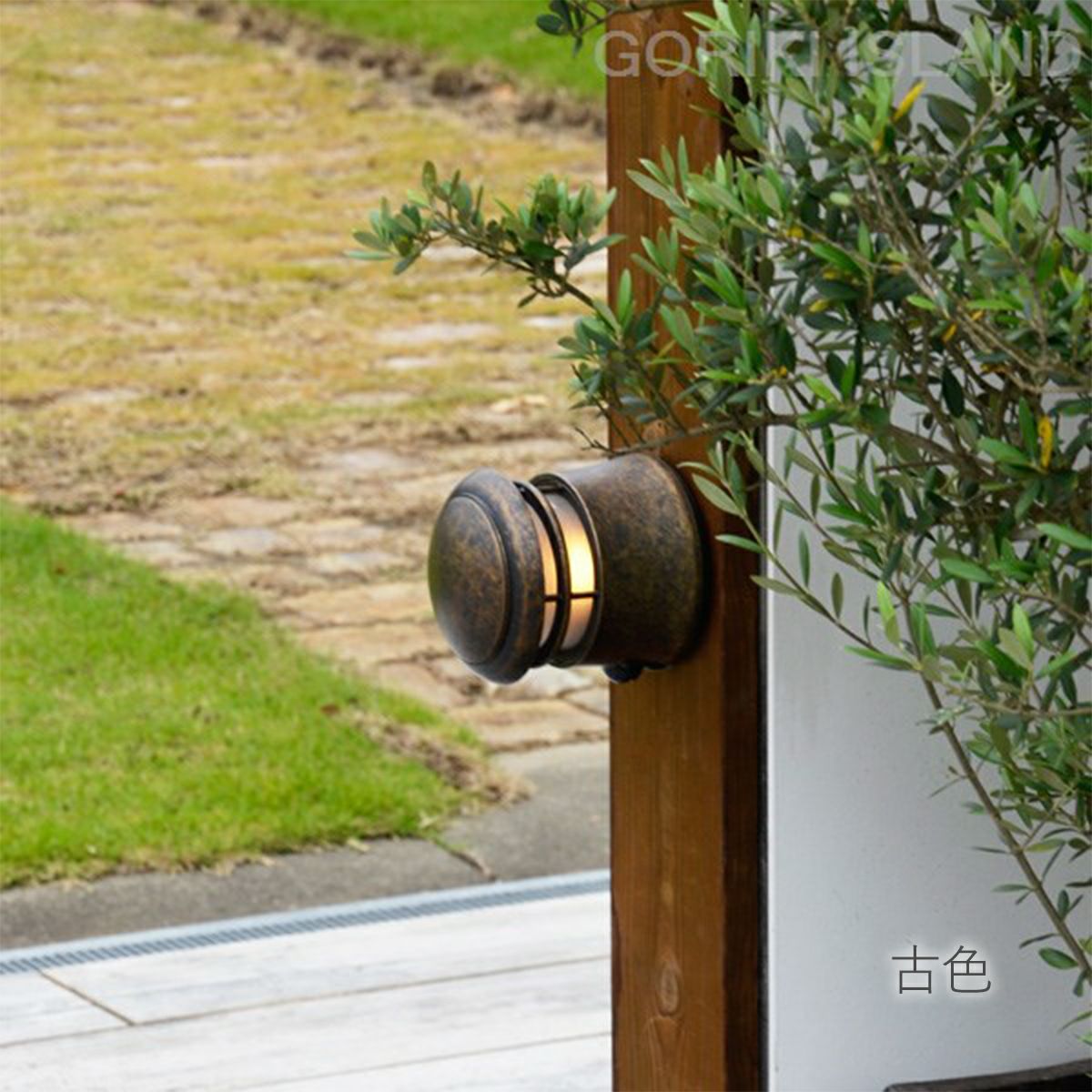 木目調の住宅の柱に、古色のライトが取り付けられている。ライトのガラスはくもっていて中の電球が見えない。