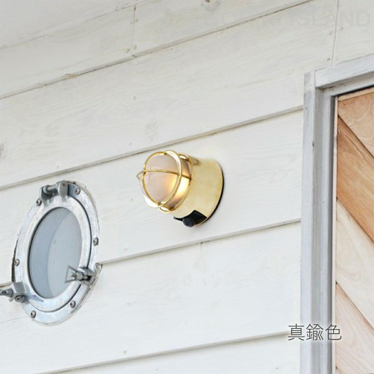 ホワイト色の住宅の外壁に、真鍮色のライトが取り付けられている。ライトのガラスはくもっていて中の電球が見えない。