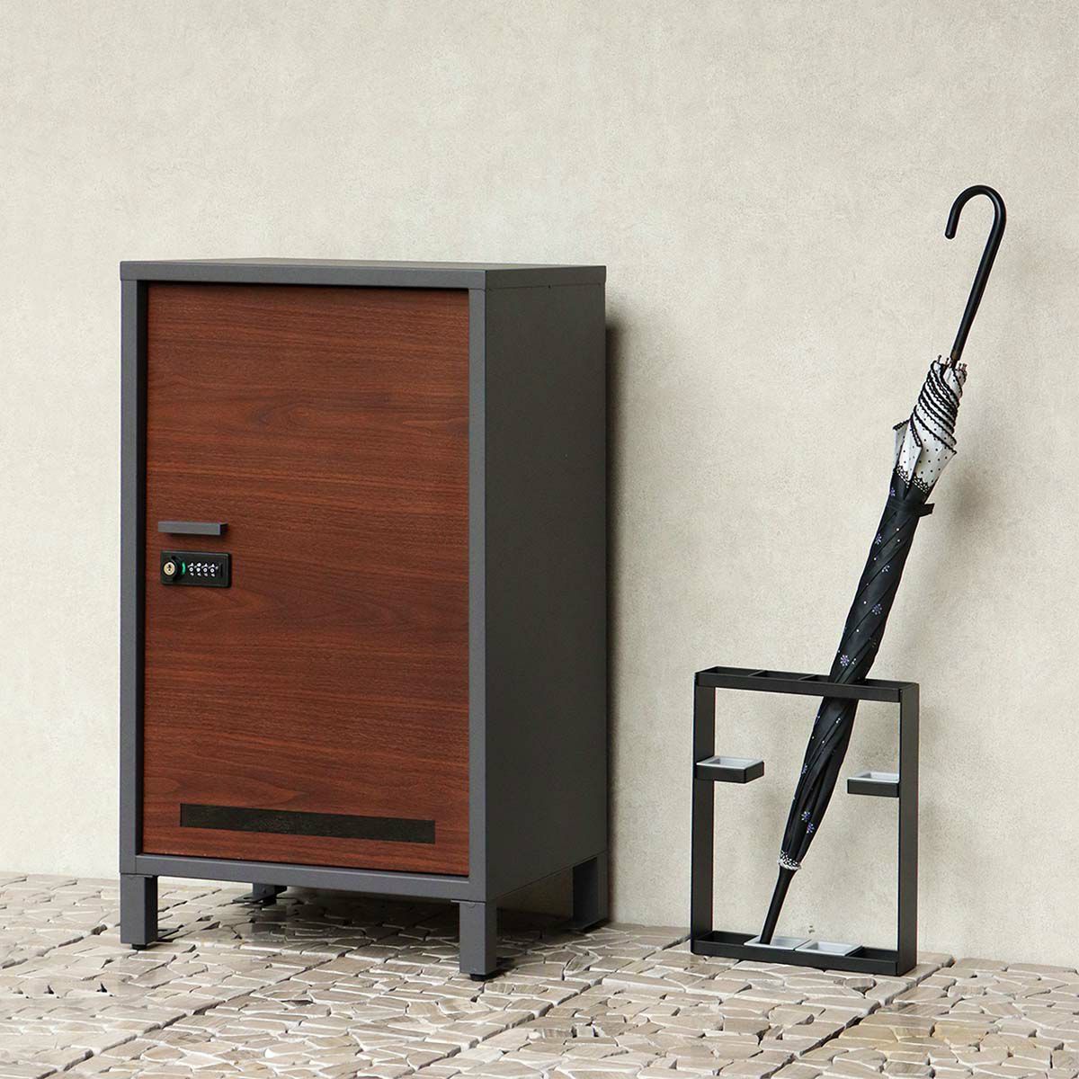 ダークグレーの宅配ボックスの設置イメージ。傘立てと並べて玄関先に置いた時のイメージ。