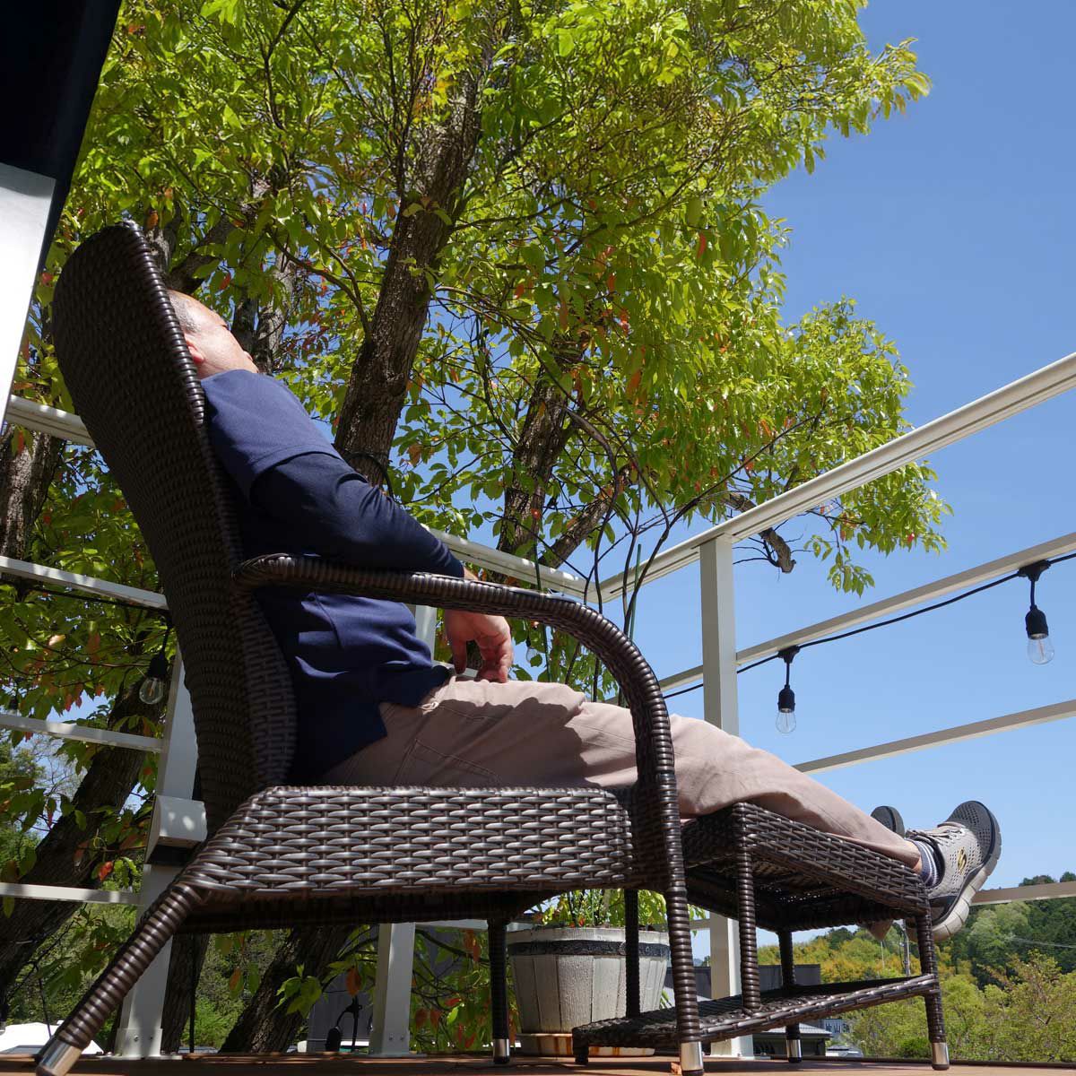 屋外デッキで男性がチェアに座ってレッグレストに脚をのせてくつろいでいる画像。